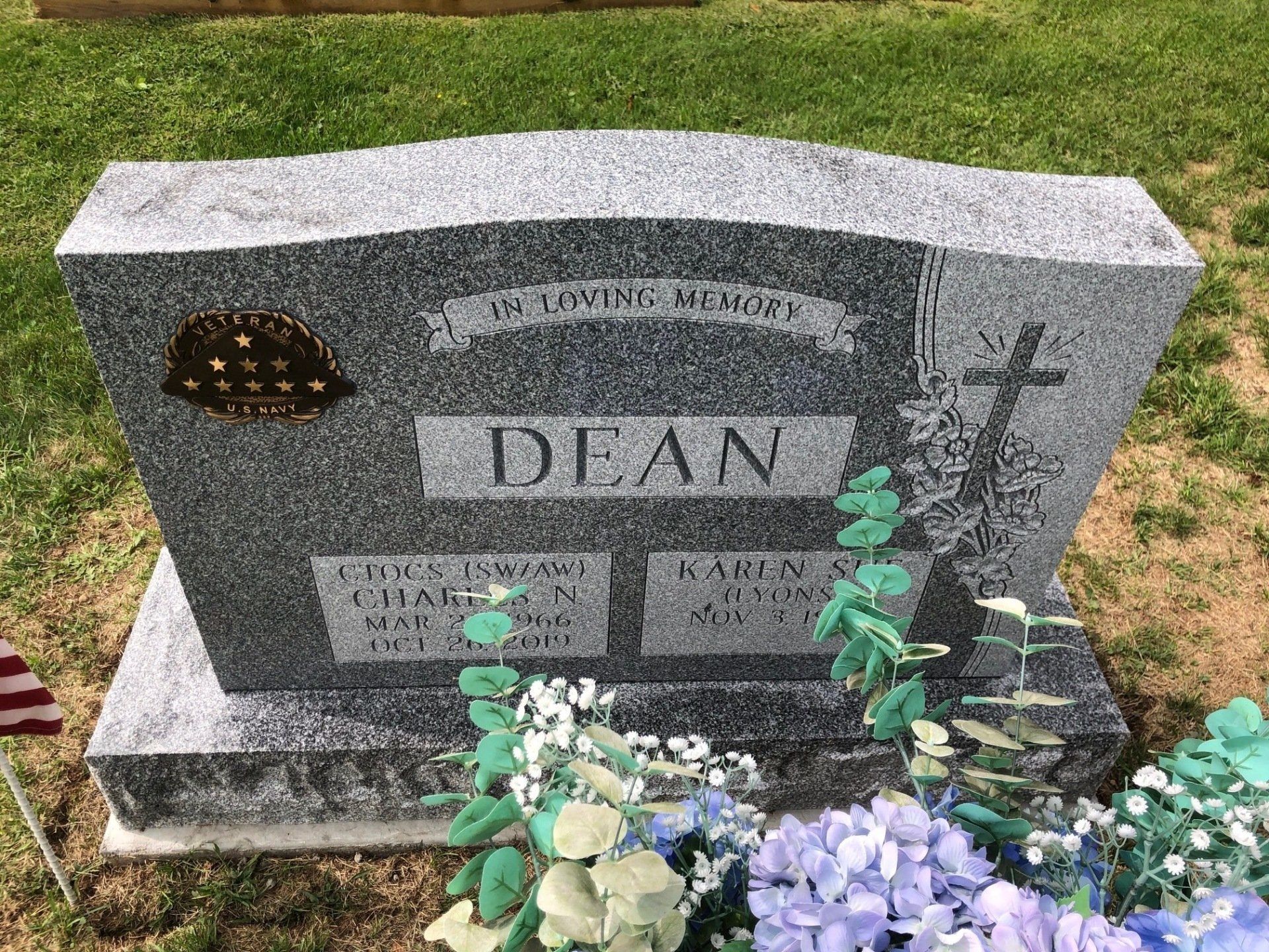 A gravestone in a cemetery with flowers and a cross on it.