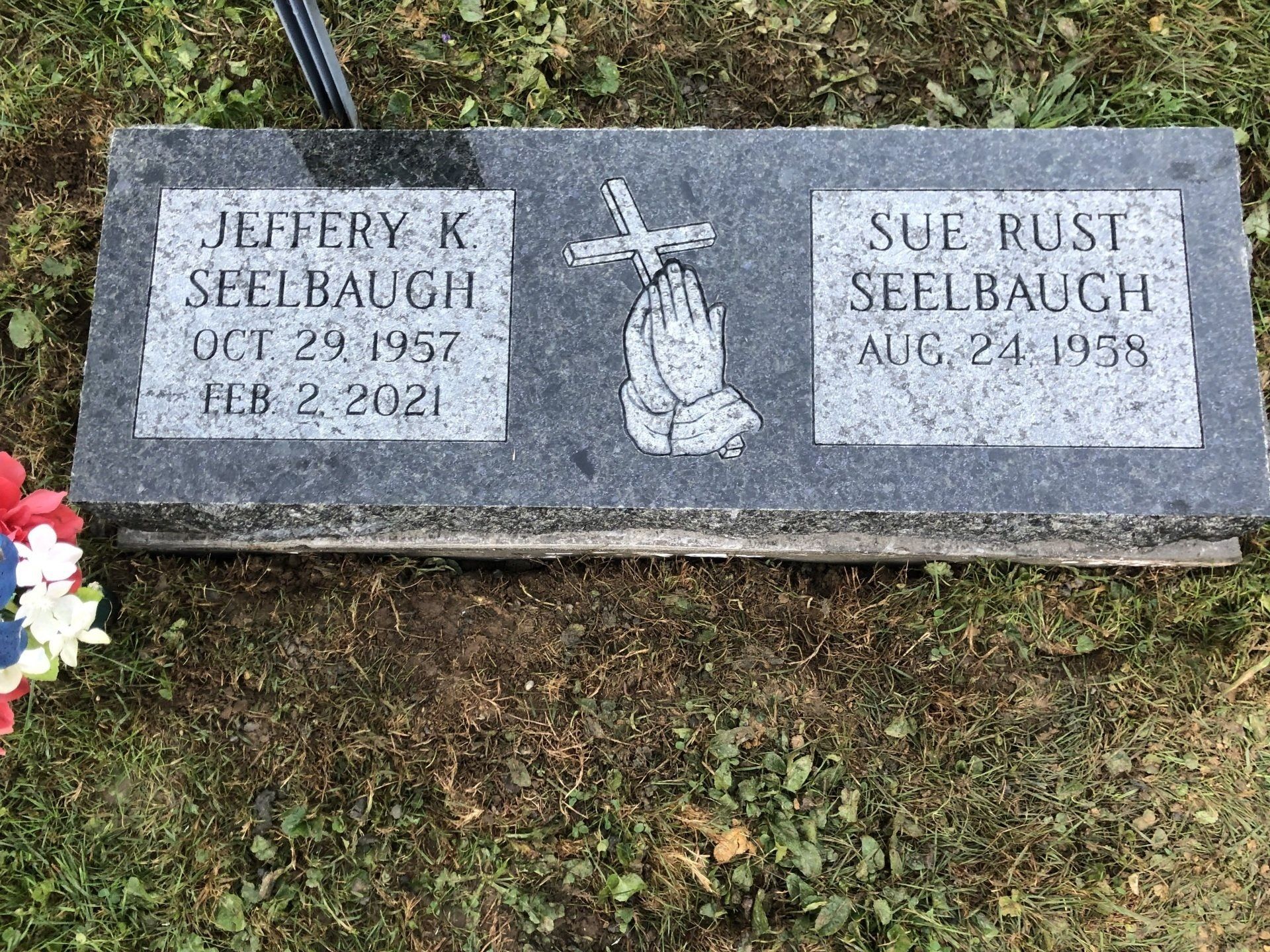 A gravestone with a cross and praying hands on it in a cemetery.