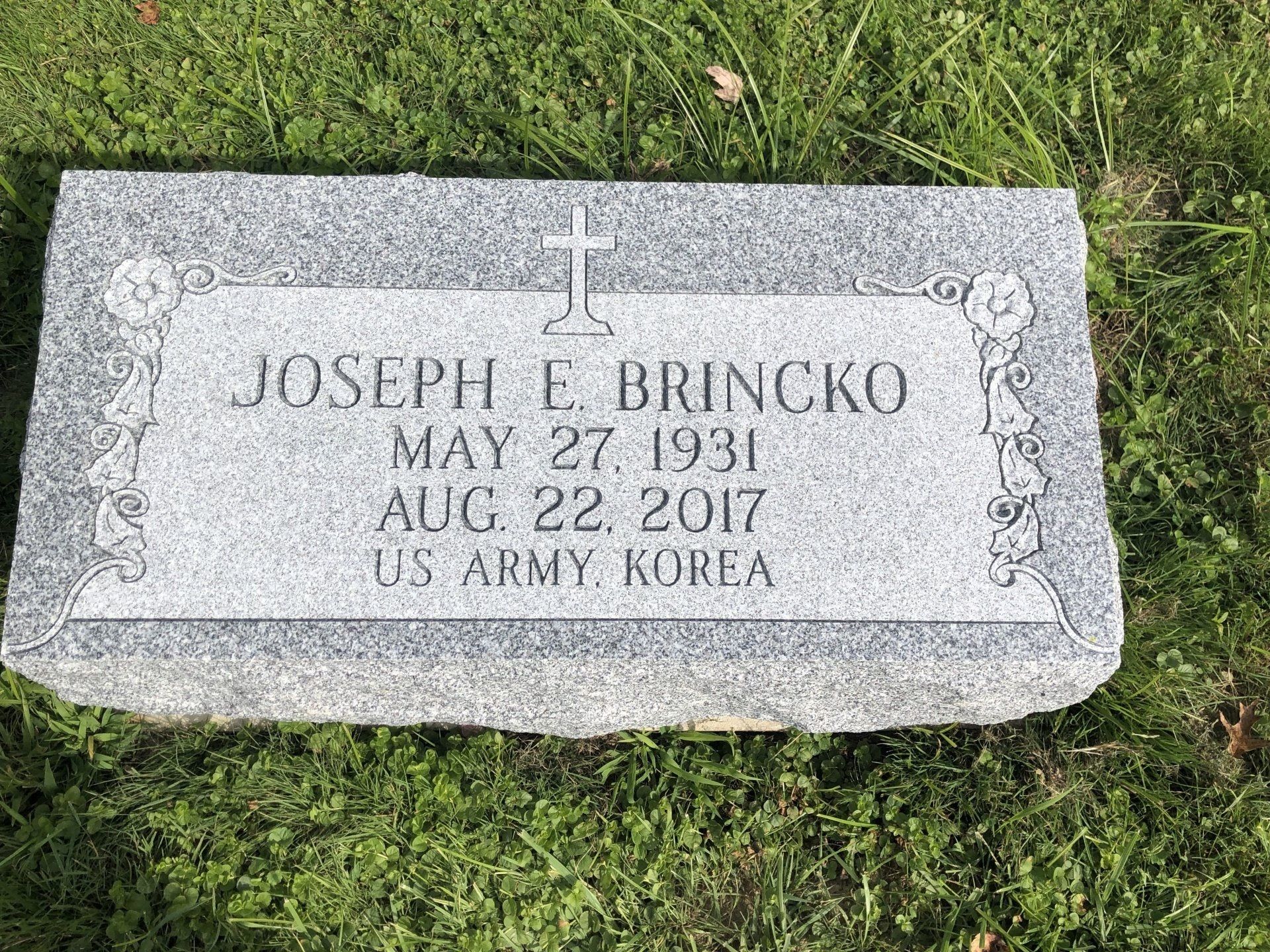 A gravestone for joseph e brincko is sitting in the grass.