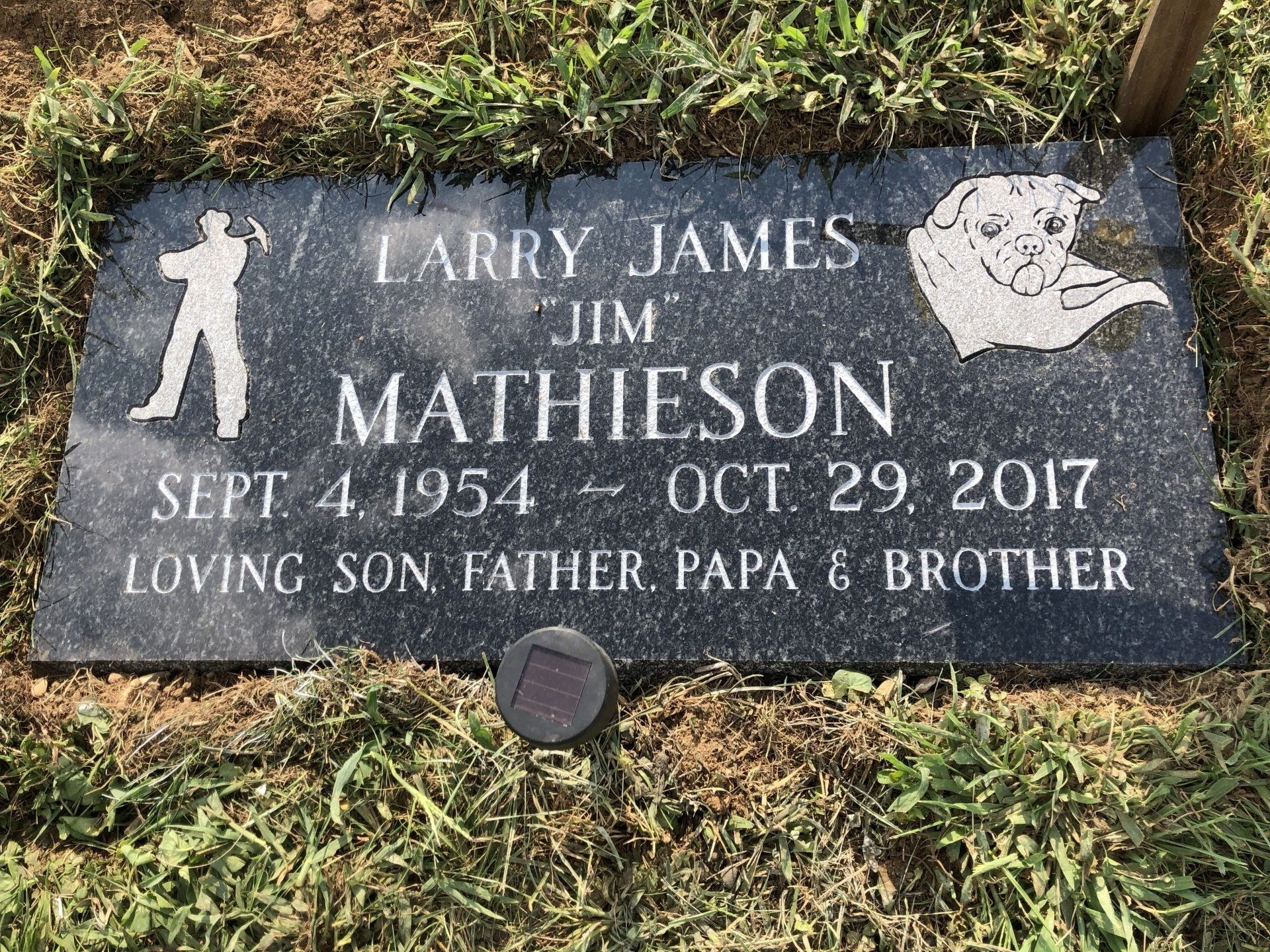 A gravestone for a man named larry james is in the grass.