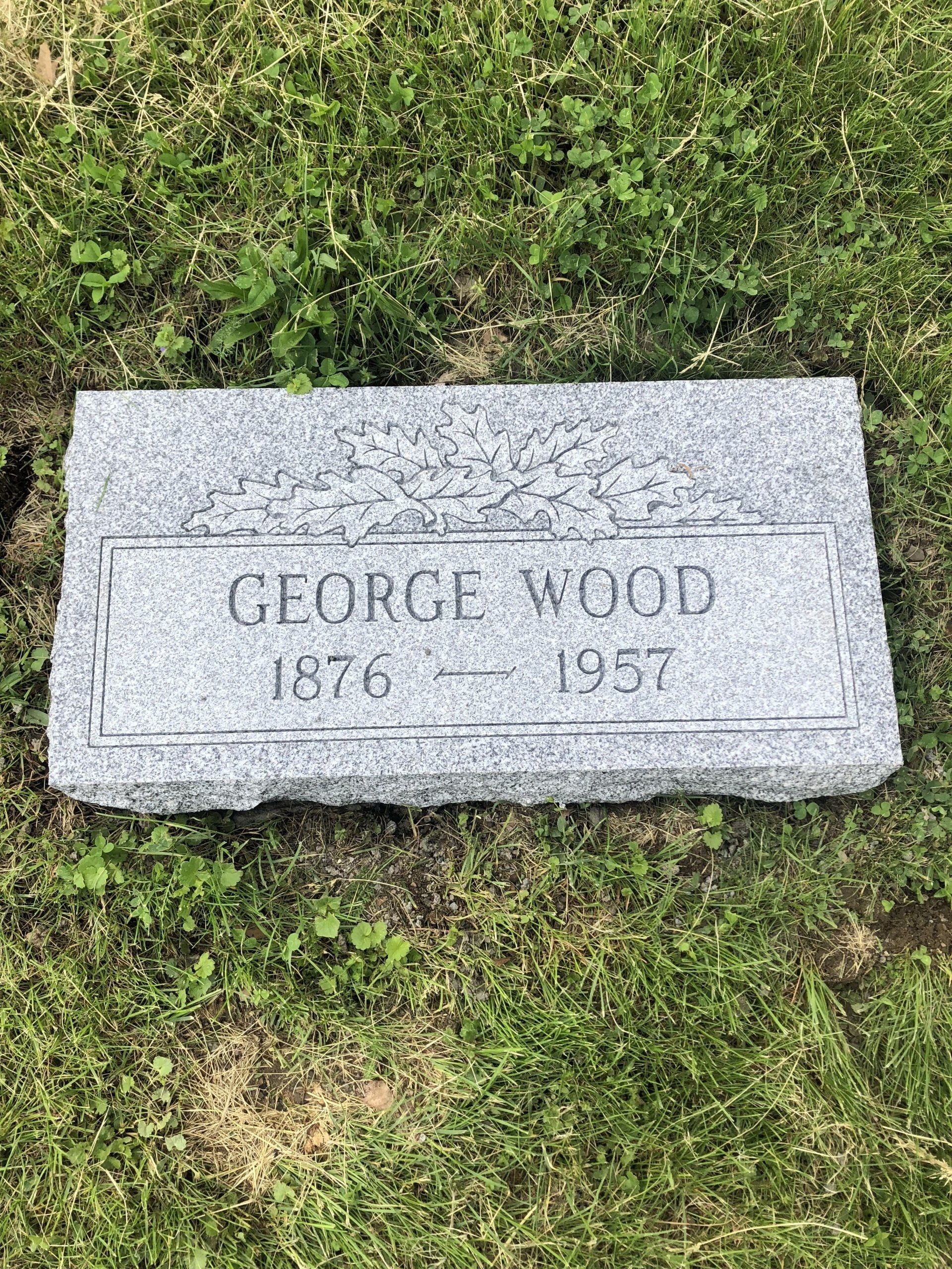 A gravestone for george wood is sitting in the grass.
