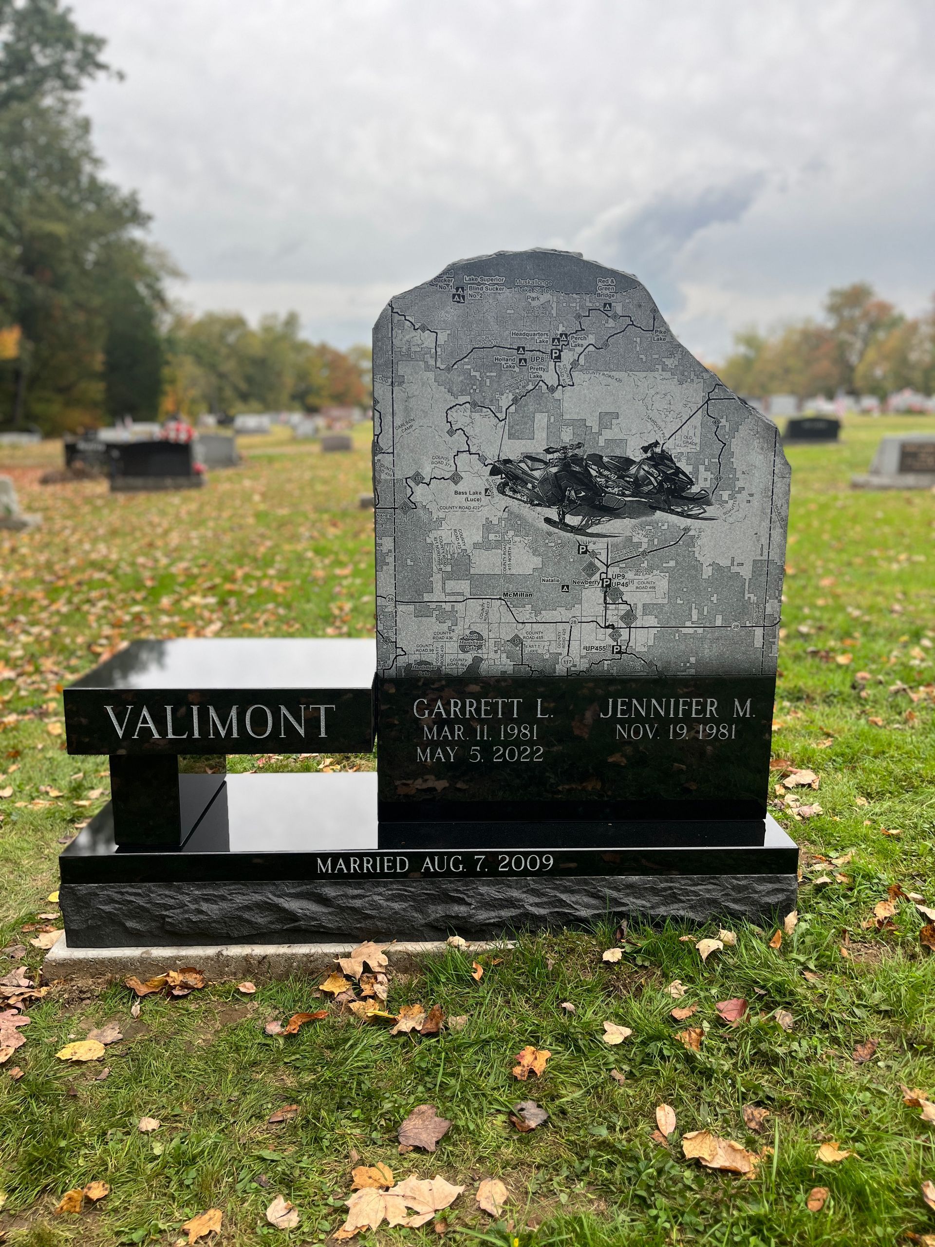 A black gravestone with a bench in a cemetery.