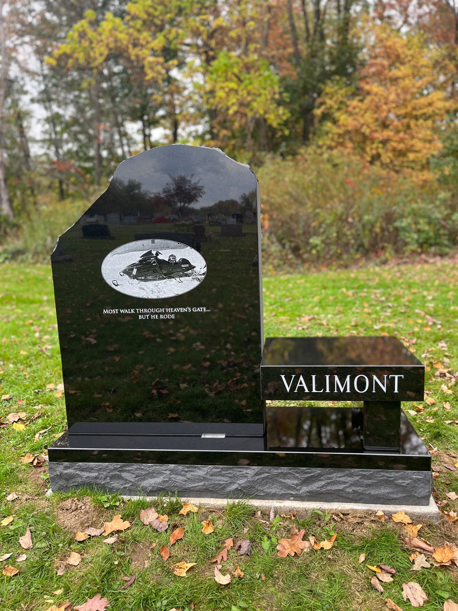 A black gravestone with a bench in a cemetery.