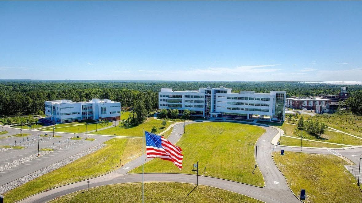 Aerial view of a campus with several buildings, a large American flag, and surrounding open green space.