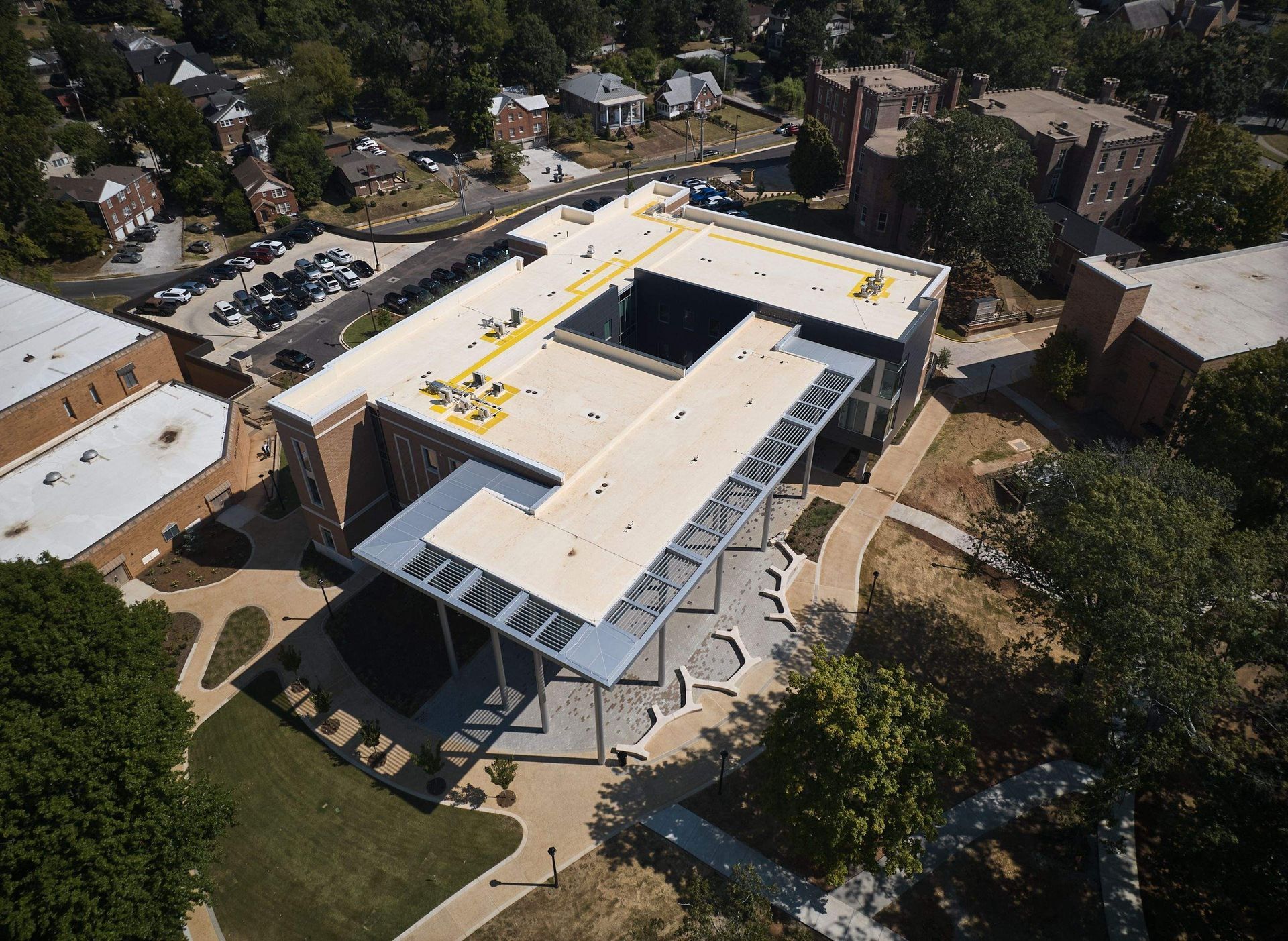 Aerial view of a modern building with a flat roof, surrounded by trees and nearby houses