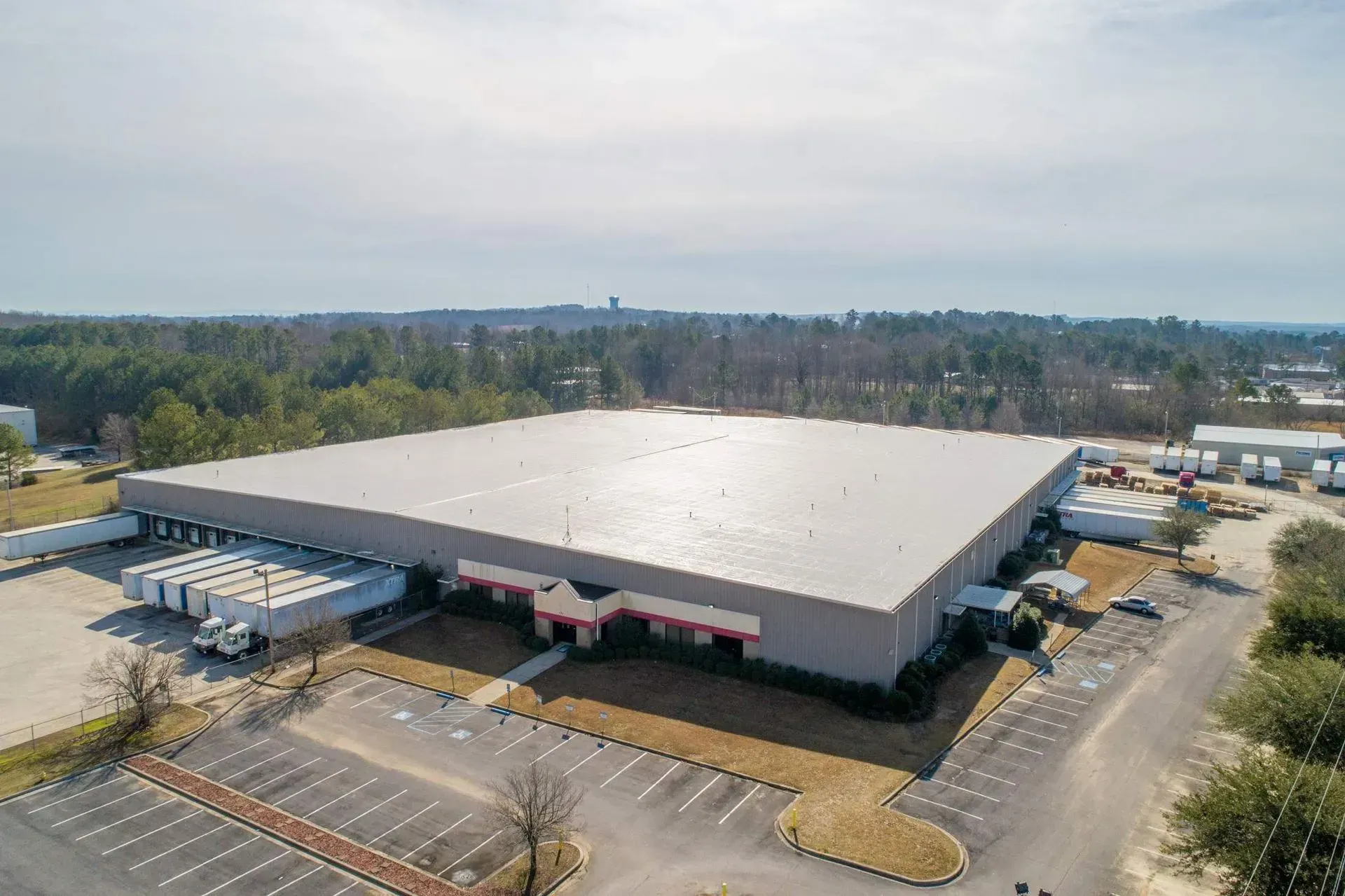 Aerial view of a large warehouse building with a white roof and parking lots surrounding it.