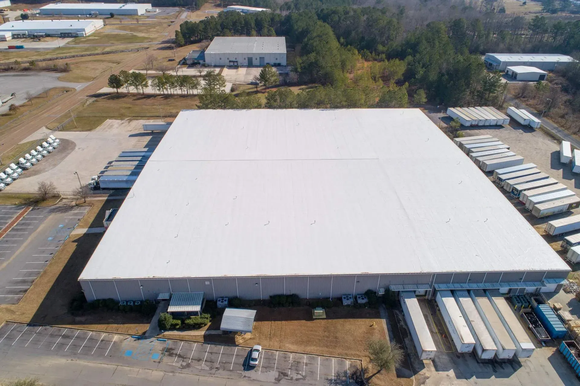 Aerial view of a large white-roofed warehouse with parked trucks in an industrial area