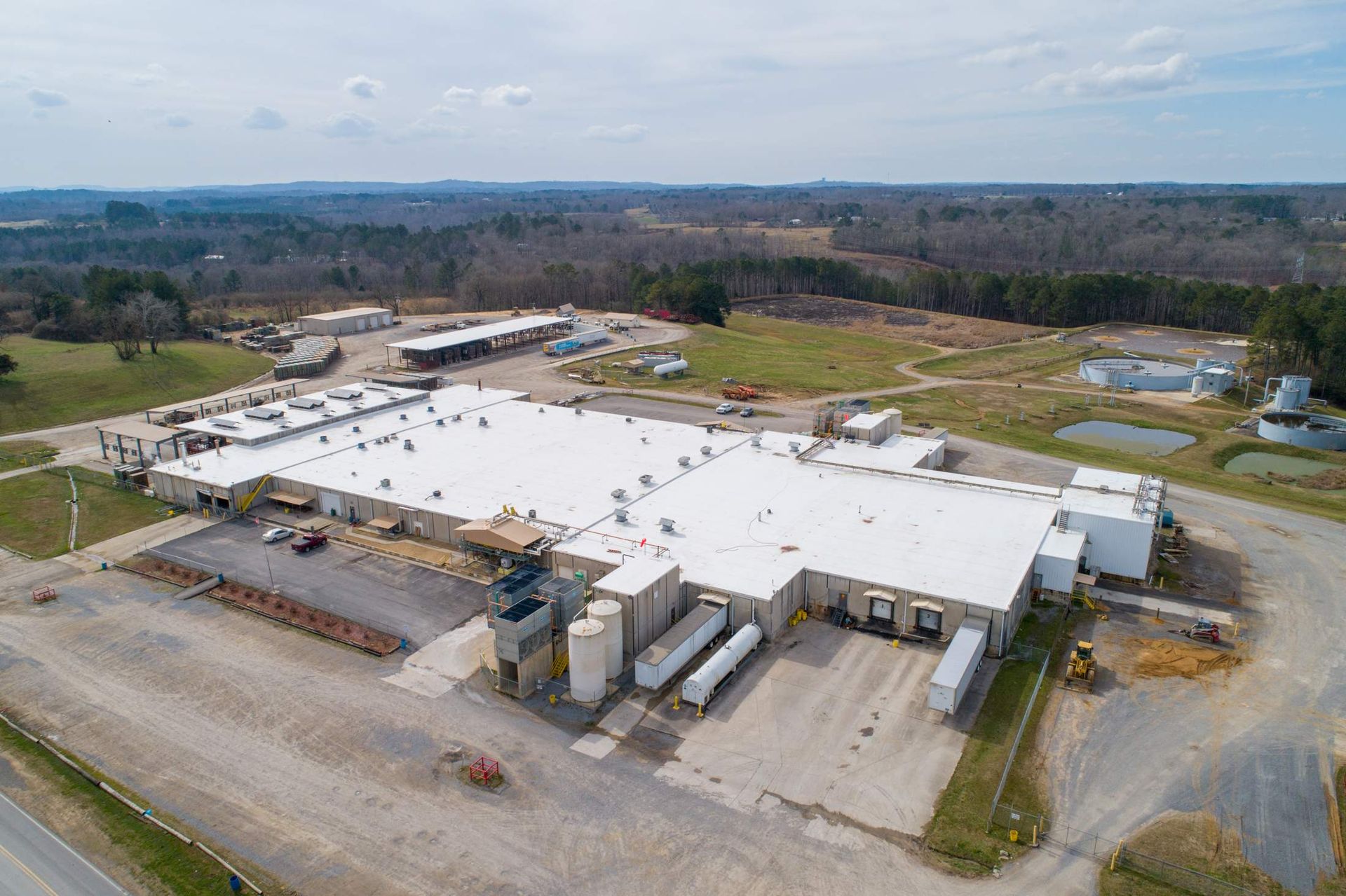 Aerial view of a large white industrial warehouse with loading docks and surrounding gravel lots.