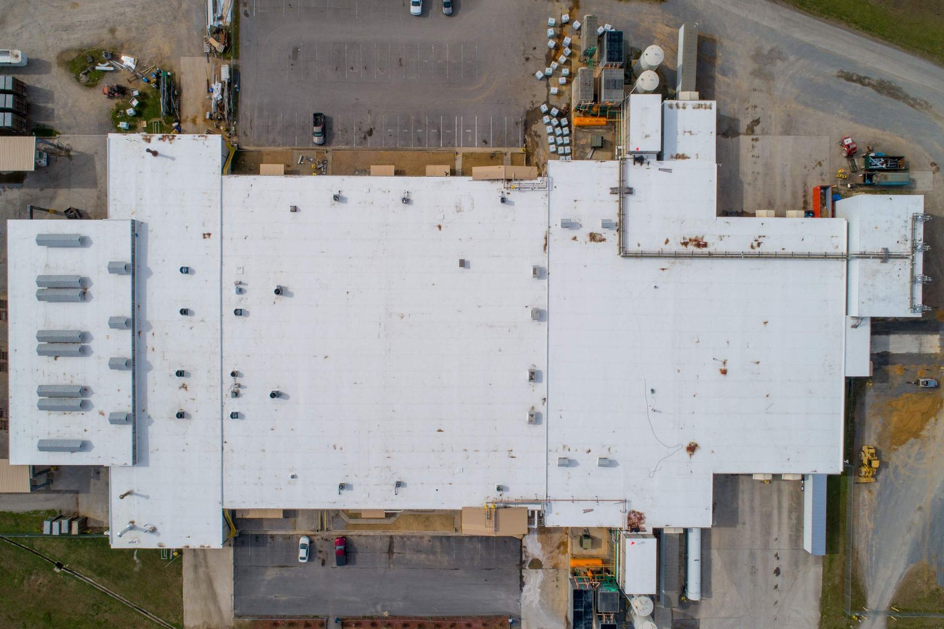 Aerial view of a large white industrial building with adjacent parking areas and surrounding roads.