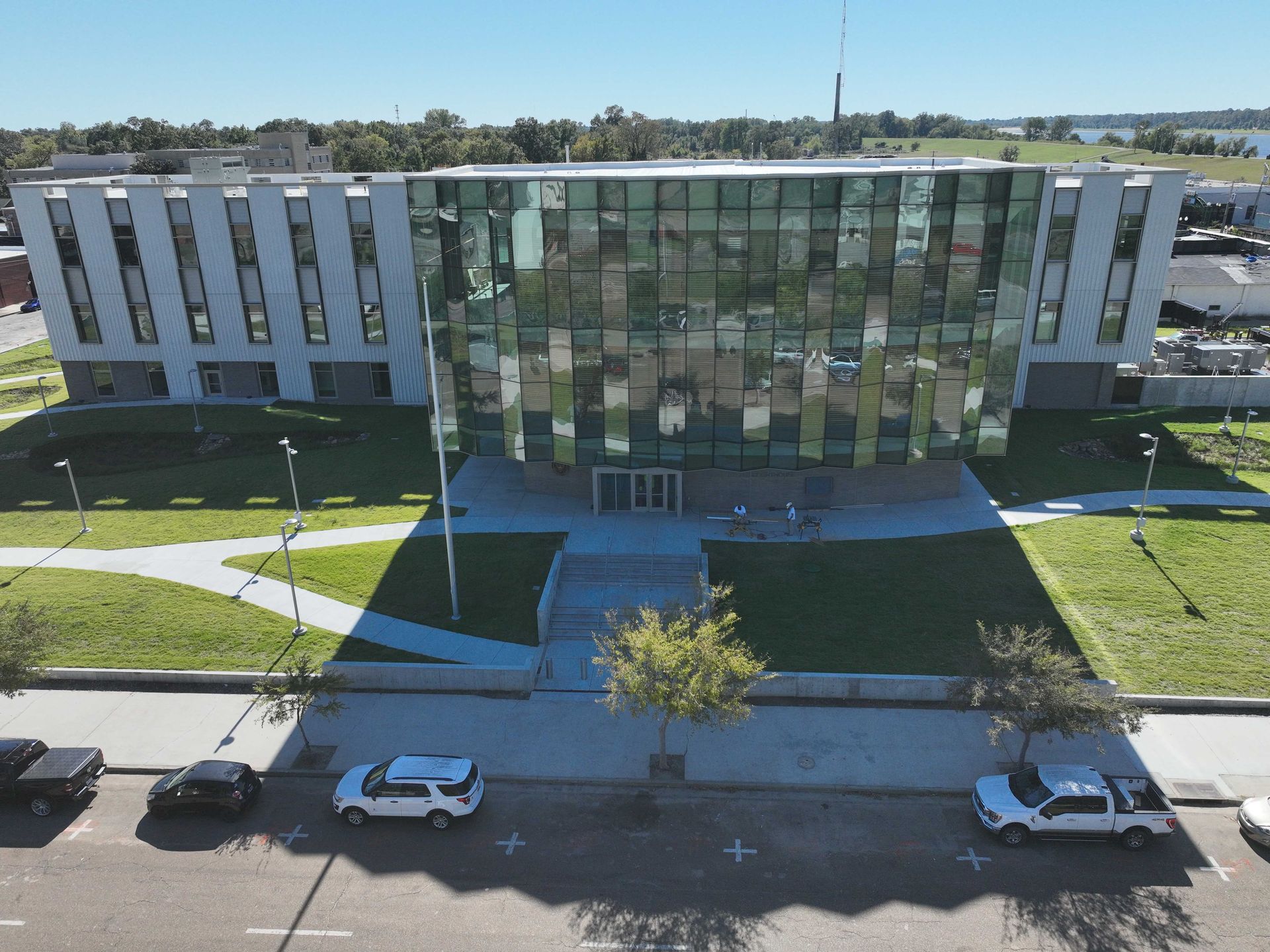 Modern office building with a glass center, white wings, front lawn, and parked cars