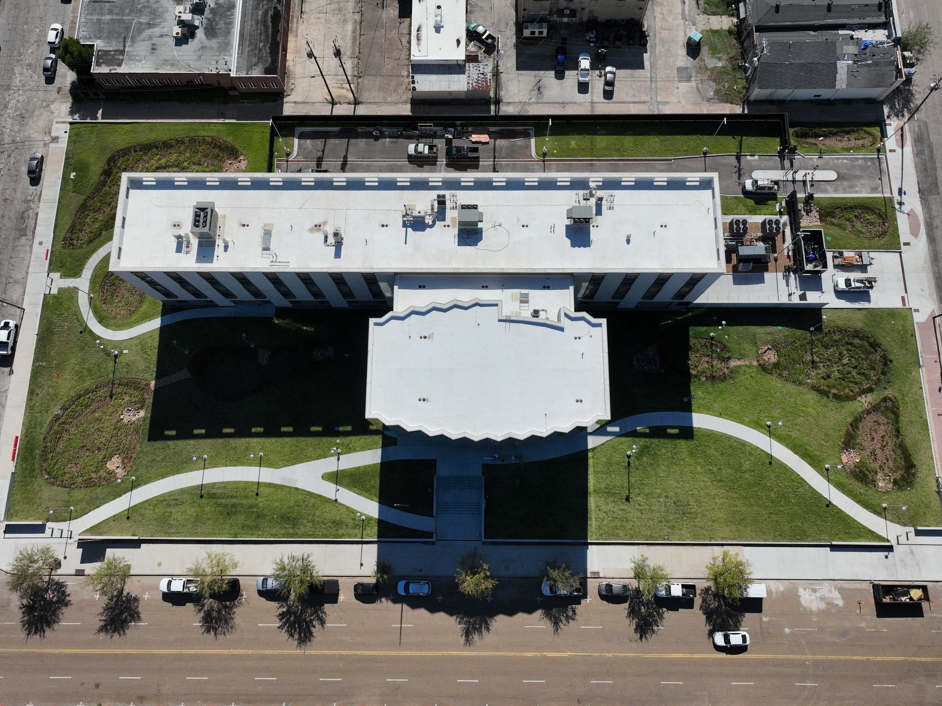 Aerial view of a modern white building with a curved entrance and surrounding lawn, roads, and parked cars.