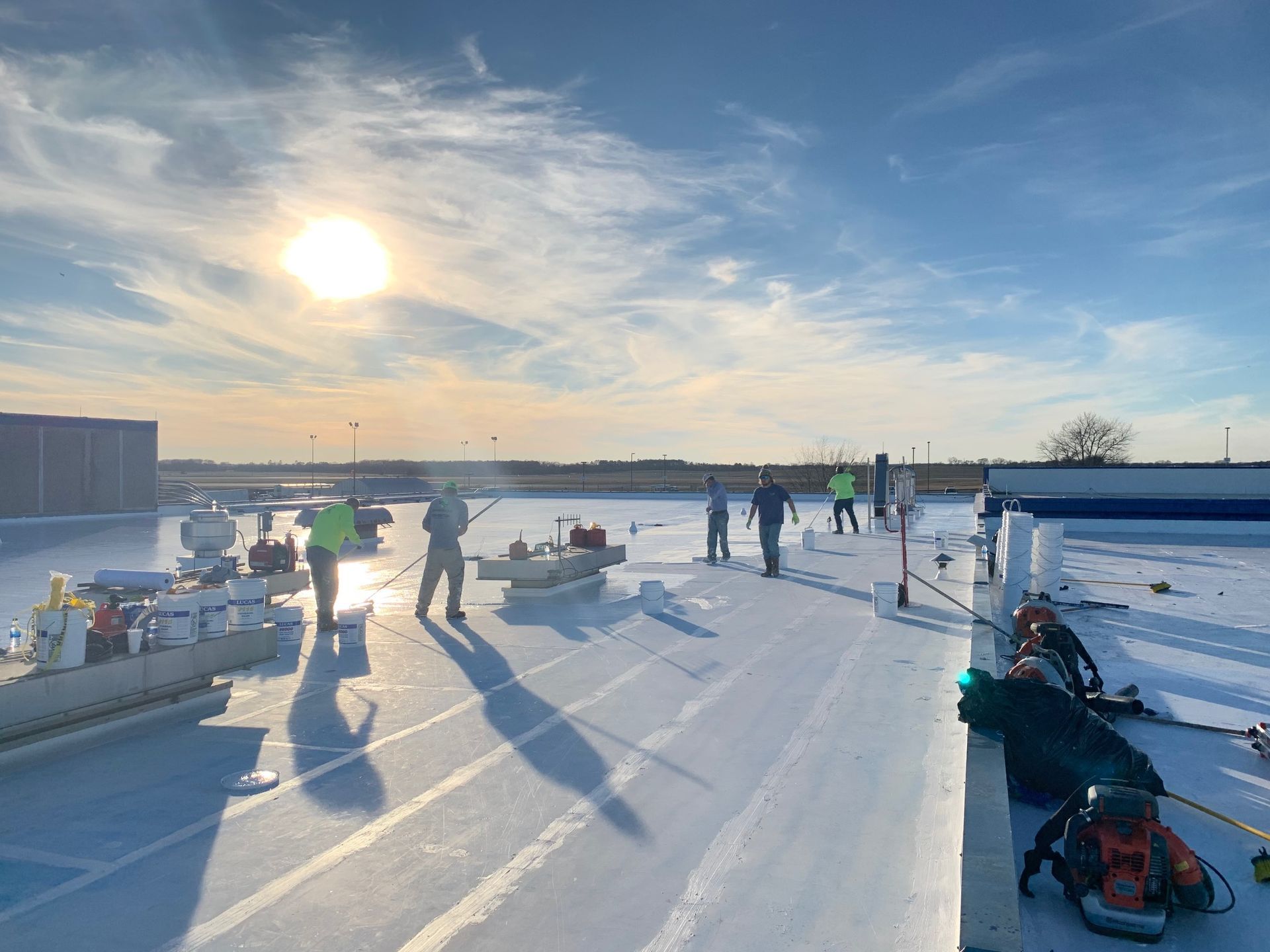 People ice fishing on a snowy lake at sunset, with long shadows and gear spread across the ice.
