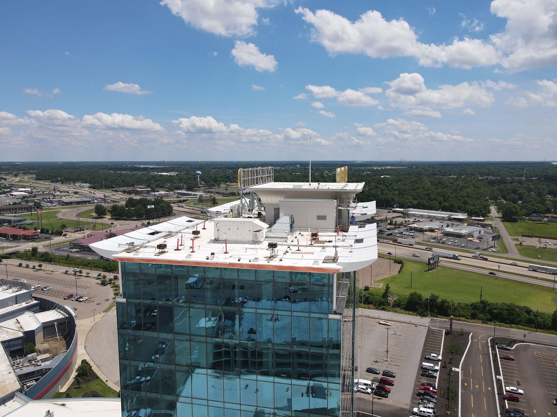 Aerial view of a glass office tower with a white rooftop under a blue sky with clouds