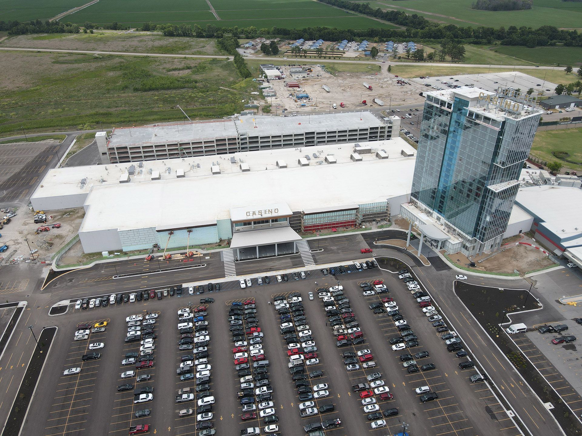Aerial view of a large shopping mall with a packed parking lot and a blue glass tower beside it