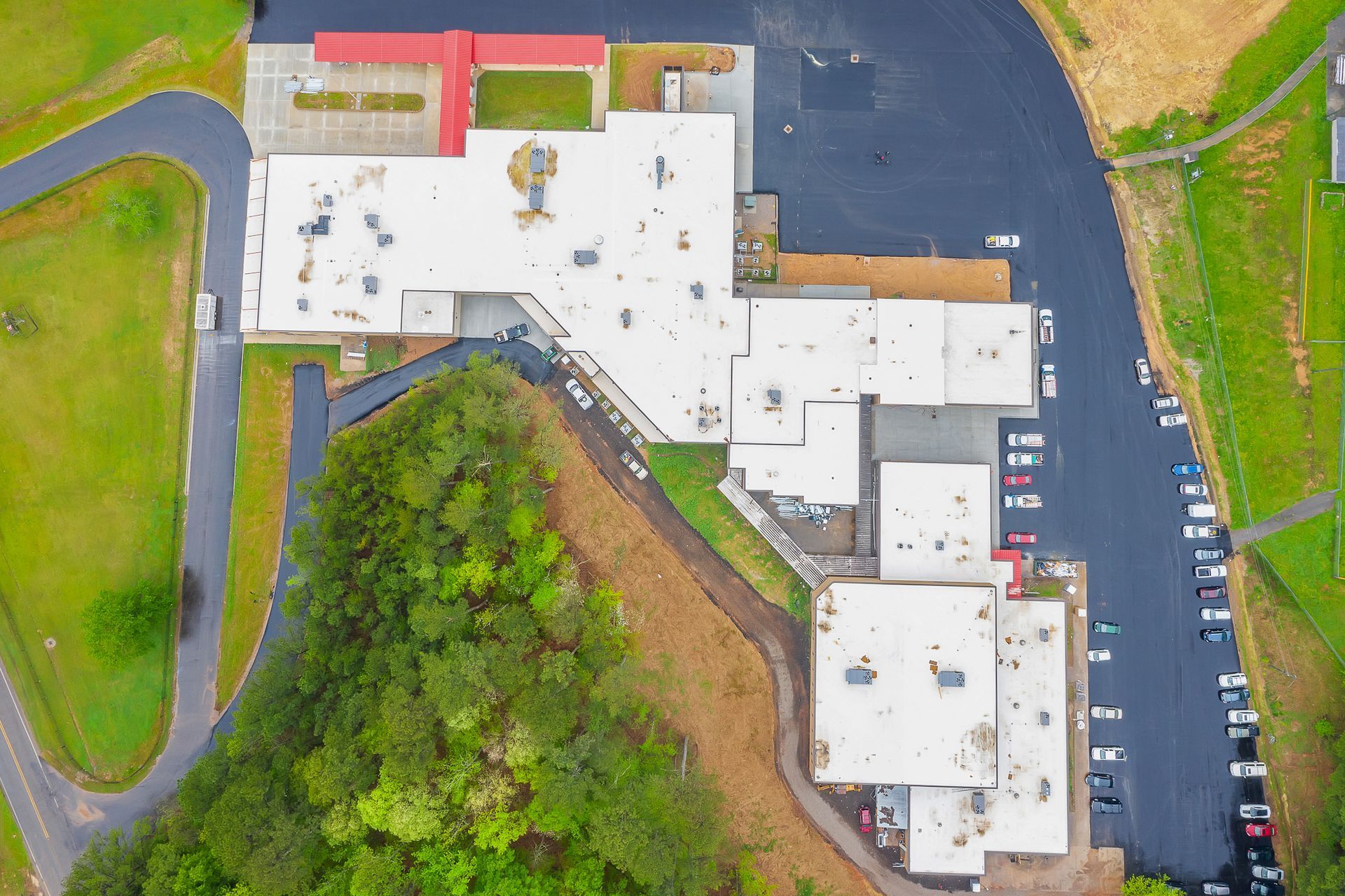 Aerial view of a large white building beside a parking lot and green fields.