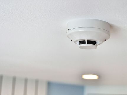White ceiling smoke detector near a recessed light in a plain indoor room