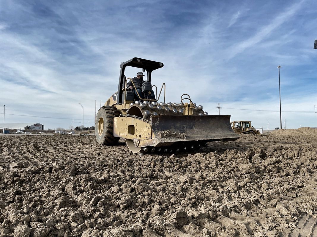 Yellow bulldozer compacting dirt on a construction site under a blue sky.