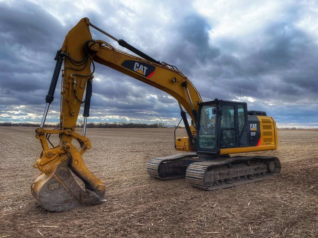 Yellow Caterpillar excavator in a field under a cloudy sky.