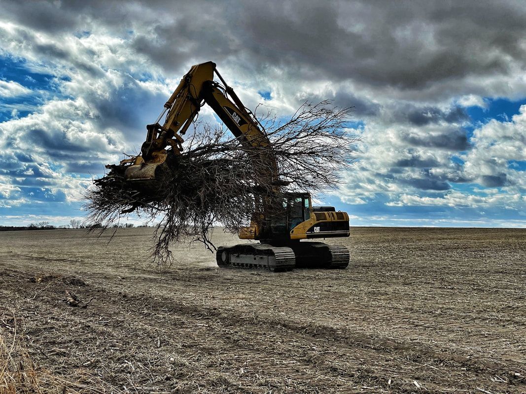 A yellow excavator tossing debris in a barren field under a cloudy sky.