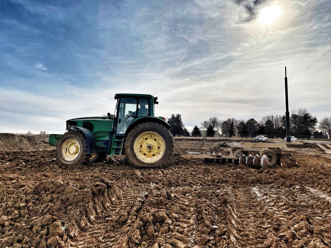 Green tractor plowing a muddy field under a bright sun.
