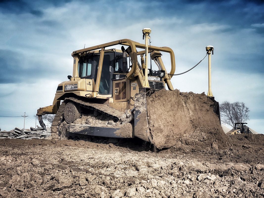 Yellow bulldozer pushing earth on a construction site; overcast sky in the background.