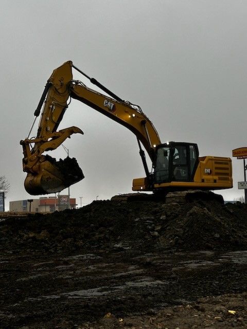 Yellow CAT excavator digging in a muddy construction site under a gray sky.