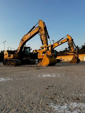 Two yellow Caterpillar excavators parked on a gravel lot under a blue sky.