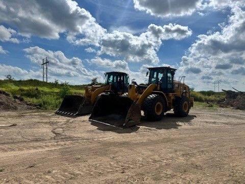 Two yellow front-end loaders parked on a dirt lot under a cloudy blue sky.