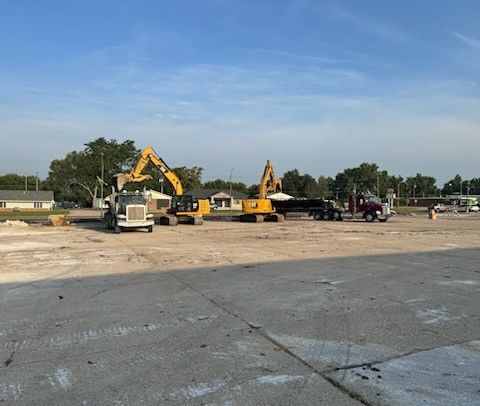 Construction site with heavy machinery, trucks, and flat, open land under a blue sky.