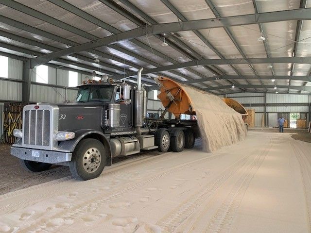 Truck hauling large, tan, cylindrical object inside a warehouse. Light streams in.