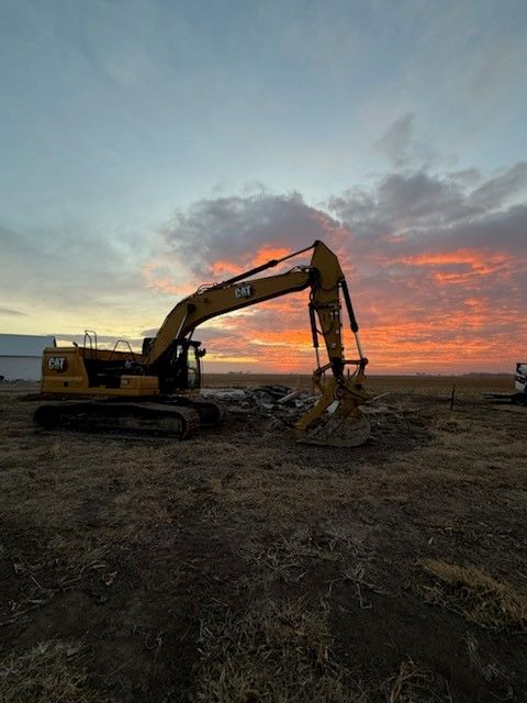 Yellow Caterpillar excavator at dusk, digging in a field with a colorful sky.