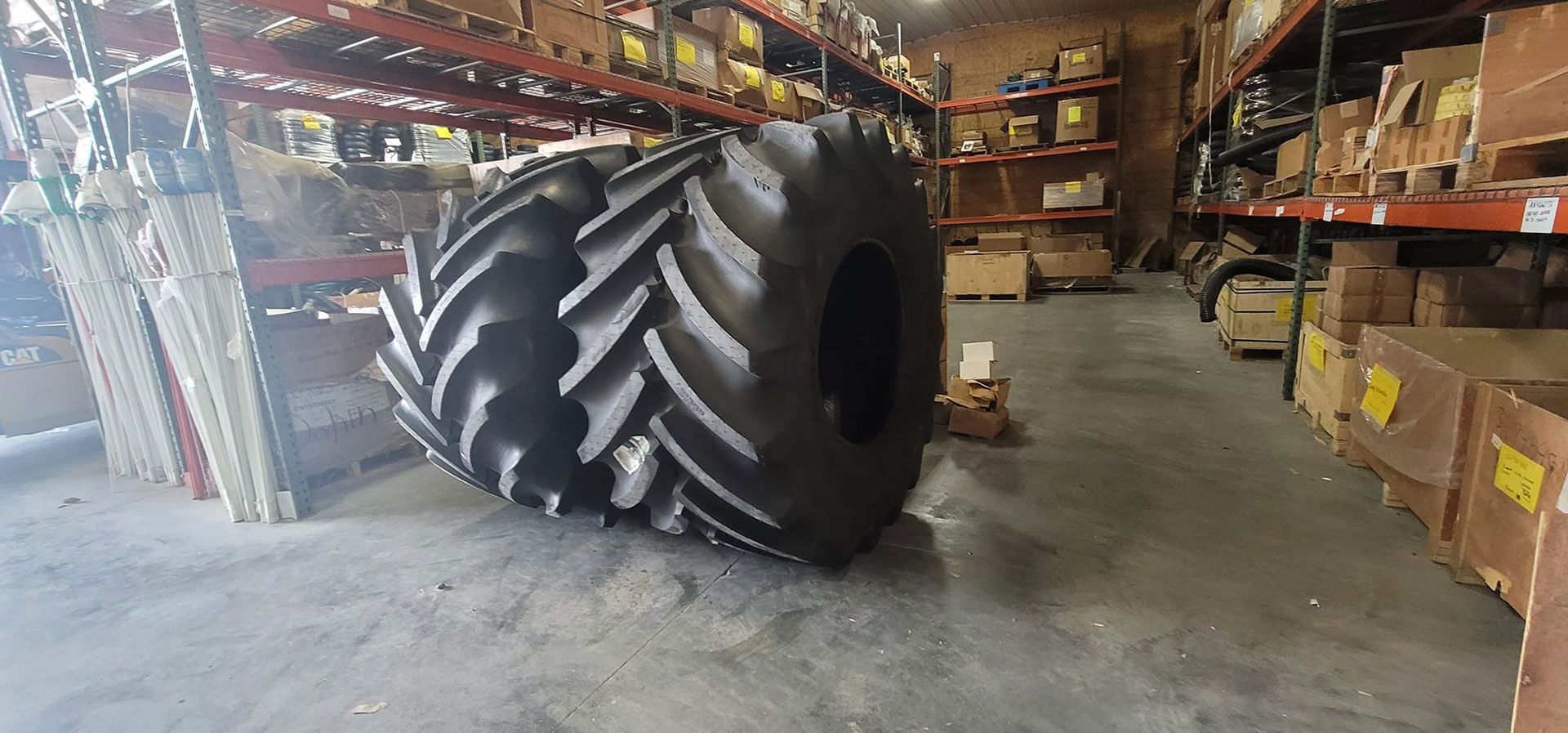 A large tractor tire sits in a warehouse with shelving, boxes, and other items.