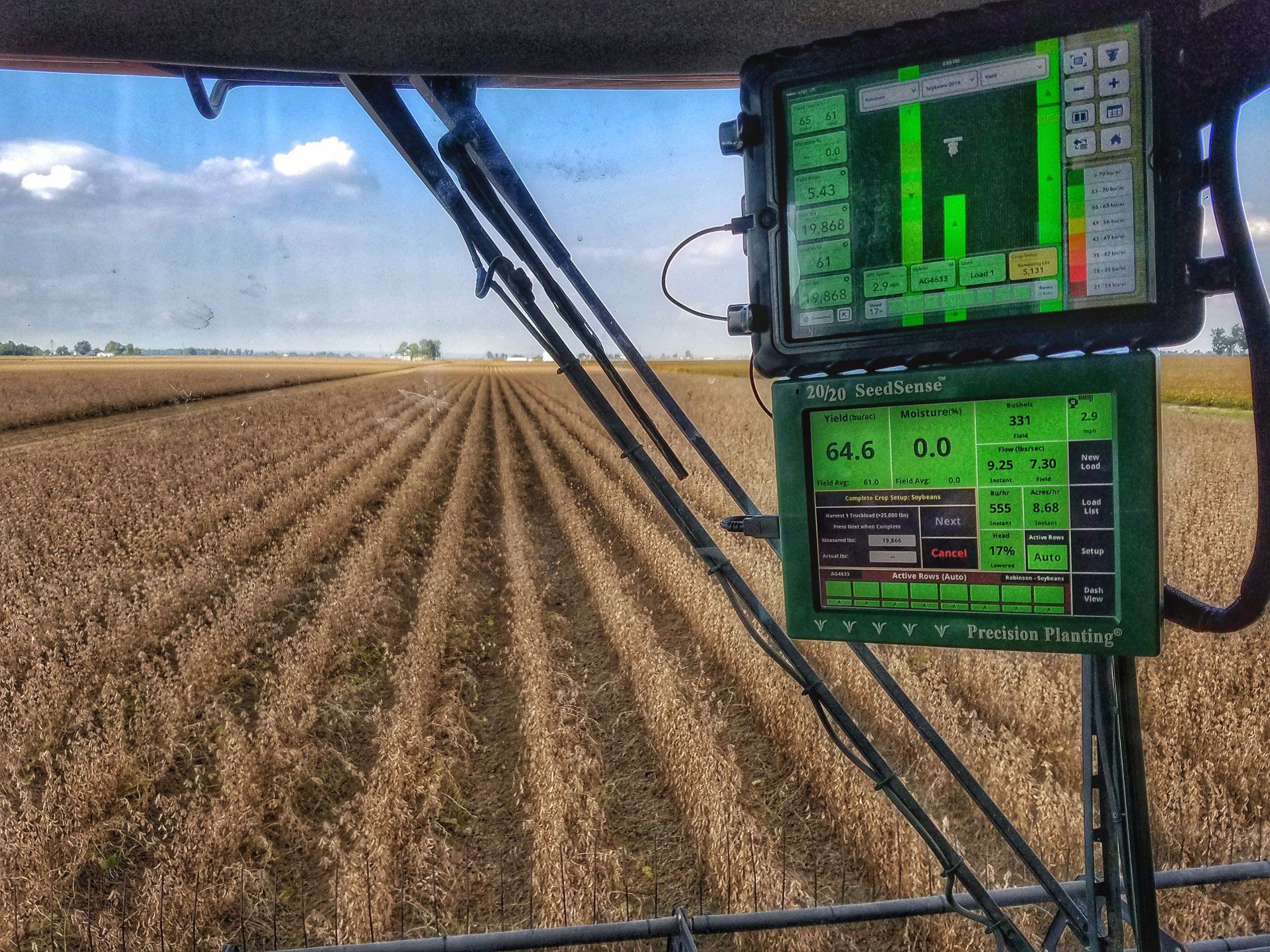View from a combine cab, harvesting crops in a field; displays show data.