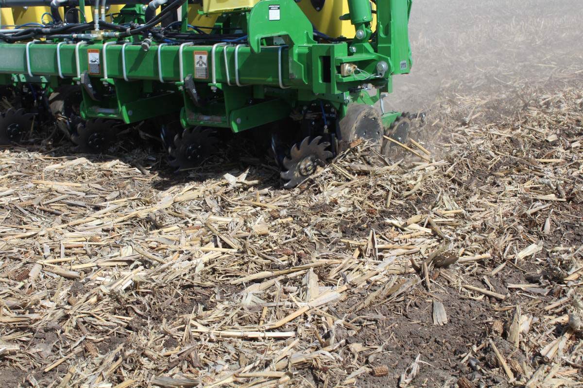 Green planter working through crop residue in a field, planting seeds.