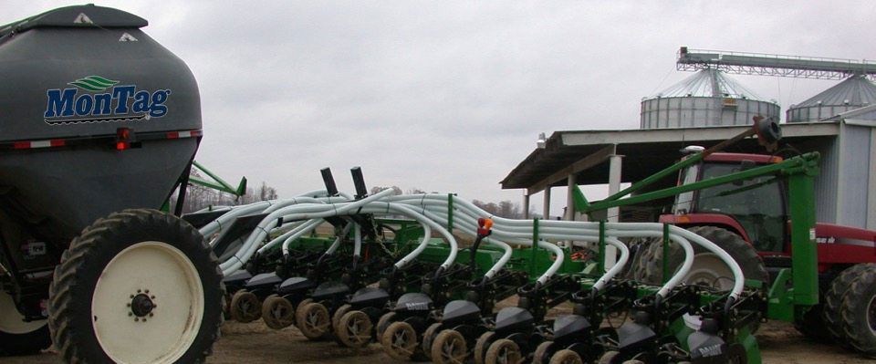 A large agricultural planter with a fertilizer tank attached to a red tractor. Cloudy sky in the background.