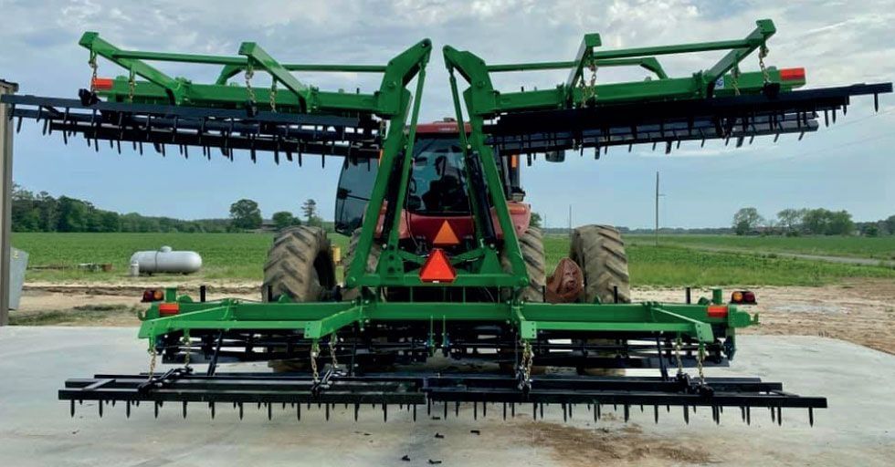 Green tractor with wide field cultivator in field.