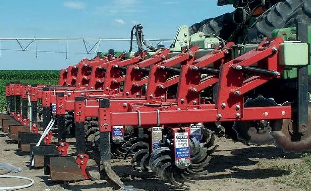 Red agricultural tillage equipment attached to a green tractor in a field.