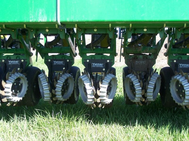Close-up of farm implement with seeders and ribbed wheels on green equipment in a field.