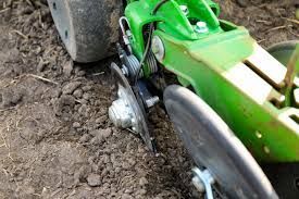 Green farm machinery, planting seeds in dark soil.