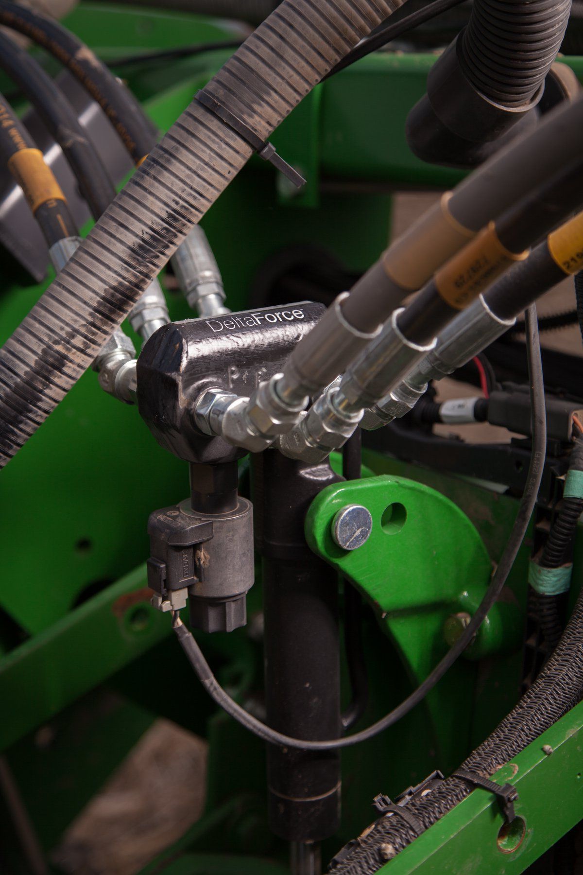 Close-up of a green farm implement with black hydraulic hoses and fittings.