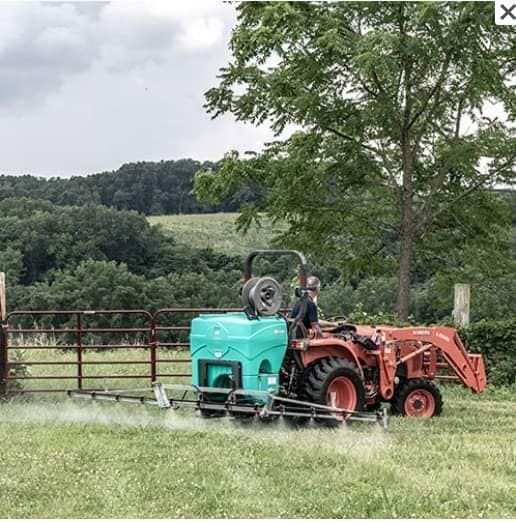 A tractor sprays a field with pesticides on a grassy field in a rural setting.