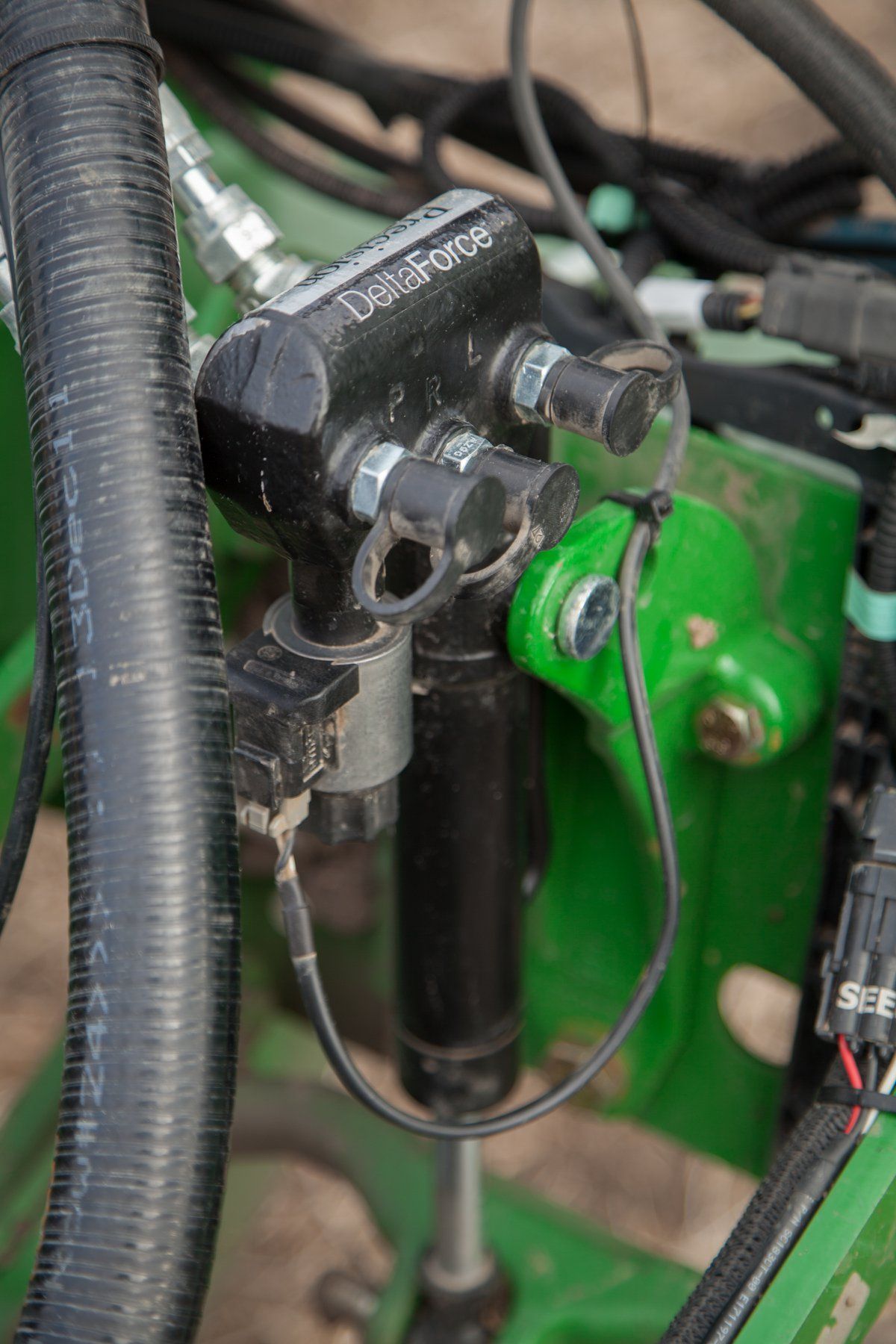 Black hydraulic control valve on a green machine, with wiring and a black hose.