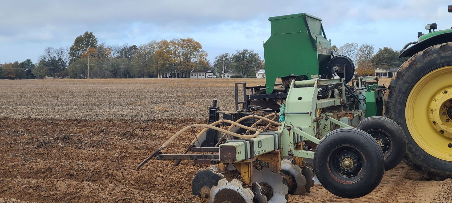 A green John Deere tractor with a planter in a field.