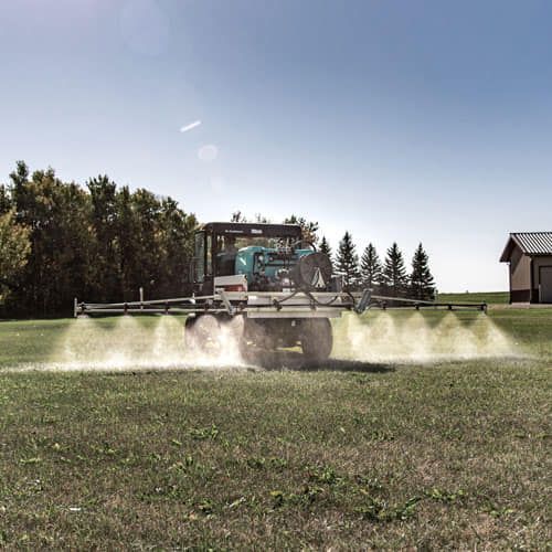 A green tractor spraying a field with a white substance on a sunny day.