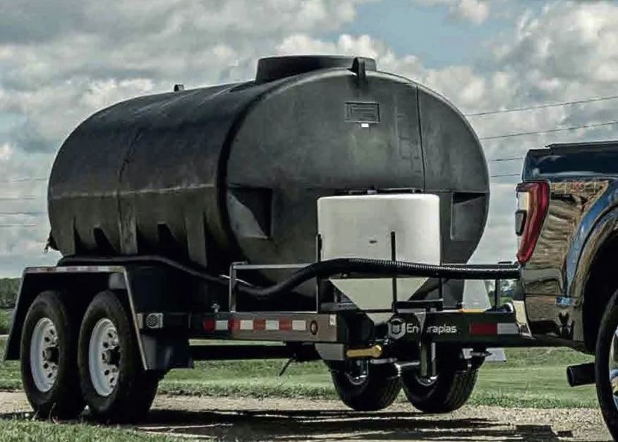 Black water tank trailer being towed by a truck on a rural road.