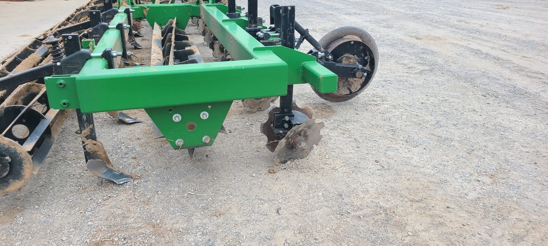 Green farm equipment tilling the soil, outdoors.