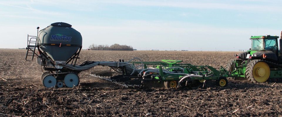 A tractor pulling a planter on a farm. Dark soil, blue sky.