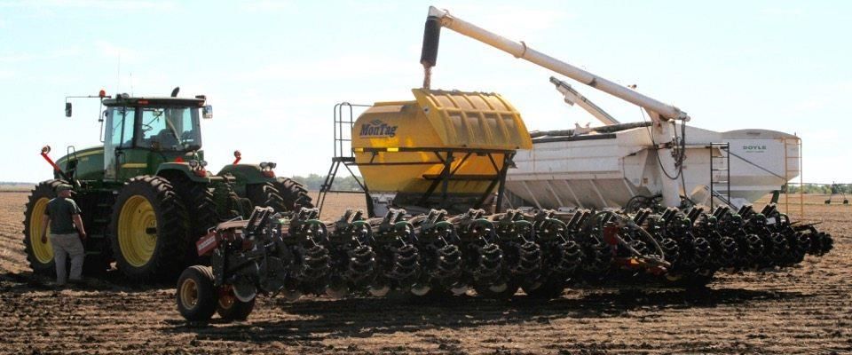 A green John Deere tractor plowing a field with a yellow planter and a white seed bin.