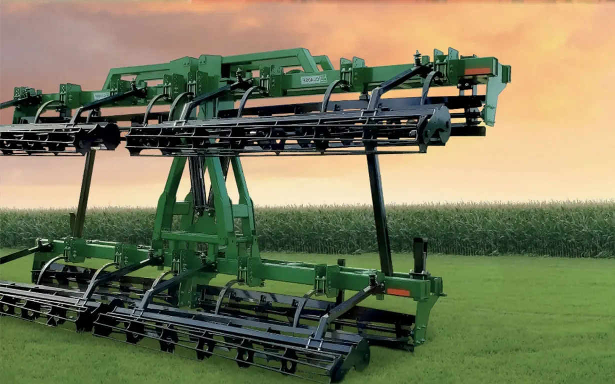 A green tractor with a planting machine working in a field. Brown soil and cloudy sky.