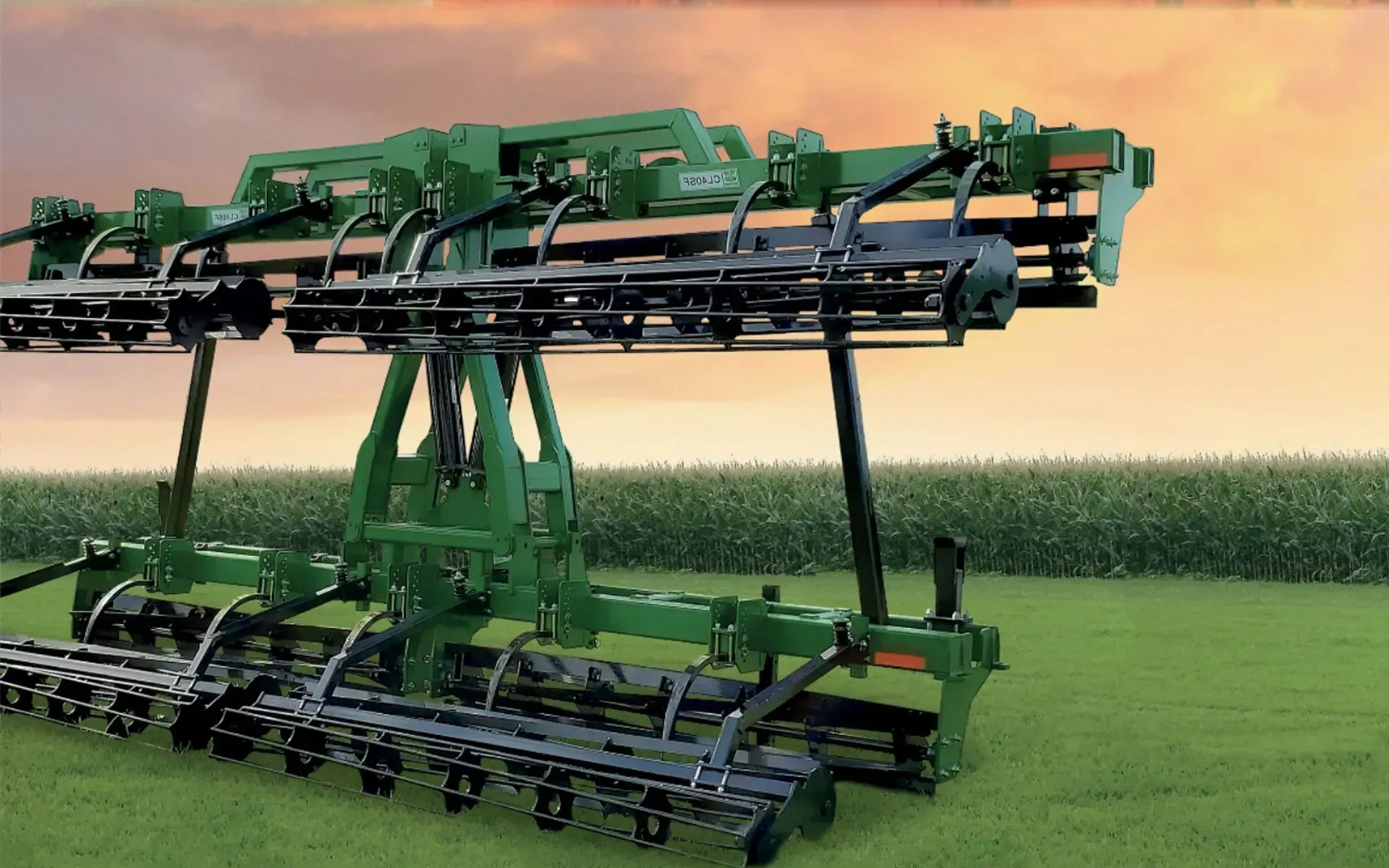 A green tractor with a planting machine working in a field. Brown soil and cloudy sky.